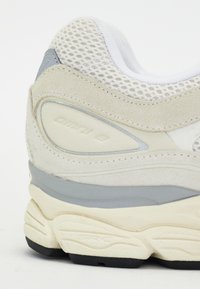 Scarpa sportiva di colore grigio chiaro con tomaia in rete, dettagli in suede e suola intermedia ammortizzata. Logo notevole sul tallone e suola testurizzata.