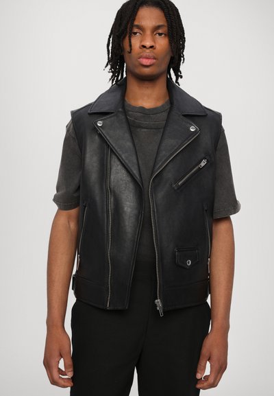 Zwarte leren vest met een gekartelde kraag, ritsen aan de voorkant en zakken, met een gestructureerde afwerking, gelaagd over een donkergrijze shirt.