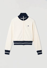 Chaqueta blanca con cremallera y cuello, puños y dobladillo de canalé azul, que presenta rayas blancas y un pequeño logo azul en el pecho.