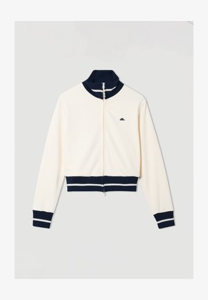 Witte zip-up jack met een marineblauwe ribbelkraag, -manchetten en -zoom, voorzien van witte strepen en een klein marineblauw logo op de borst.