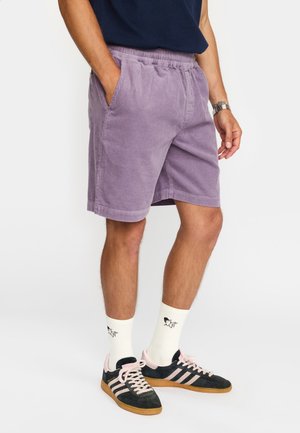 Shorts en velours côtelé violet clair avec une taille élastique, des poches latérales et des ourlets plats, assortis à des chaussettes blanches et des baskets noires.