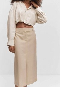 Chemise en lin beige clair, courte, à col en V et manches ballon. Jupe assortie taille haute, longueur genou, coupe droite.