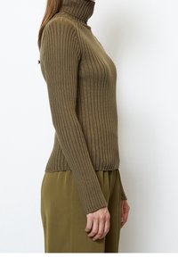 Olivově zelený žebrovaný rolák s dlouhými rukávy a přiléhavým střihem, kombinovaný s volnými olivově zelenými kalhotami. Jemná textura a elastická tkanina.