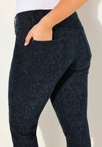 Mörkblå byxor med ett subtilt bladmönster, tillverkade av denim, med fram- och bakfickor samt en figurnära design.