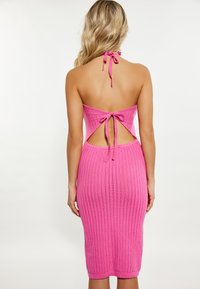 Pink ribbed knit dress with a halter neckline and open back, featuring a tie closure and body-hugging fit, ending below the knee.
