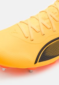Bright yellow soccer cleat with a textured surface, black accents, synthetic material, and orange outsole with silver studs.