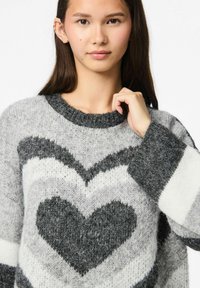 Maglione a maglia grigio e bianco con motivo a cuore e accenti a righe, caratterizzato da una texture pelosa e collo e polsini a costine.