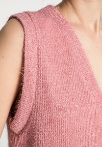 Gilet en tricot sans manches rose avec une texture douce et pelucheuse, et des fils métalliques. Dispose d'un décolleté plongeant et de larges emmanchures, offrant une bonne respirabilité.