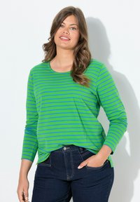 Vihreä ja sininen raidallinen pitkähihainen paita, jossa on pyöreä kaula-aukko, pehmeä tekstuuri, yhdistetty tummiin farkkuihin, kädet taskuissa.