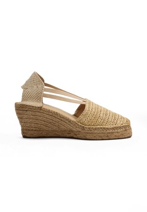 Sandalia de cuña tipo espadrille con parte superior de fibra natural tejida, puntera cerrada, contrafuerte de talón en el tobillo y tiras elásticas en tonos beige sobre fondo blanco.