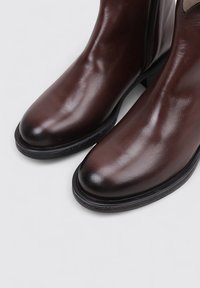 Brown leather ankle boots with a smooth, shiny finish and rounded toe; features a side zipper and a black rubber sole for grip.