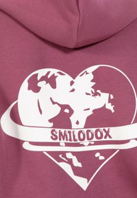 Felpa viola con un design a forma di cuore bianco su cui è raffigurato un globo e la scritta "SMILODOX" in un carattere in grassetto sottostante. Texture in cotone morbido.