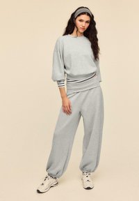 Hellgraues Sweatshirt aus Baumwolle mit Ballonärmeln, kombiniert mit passenden, weit geschnittenen Hosen. Verfügt über gestreifte Akzente an Handgelenken und Bund.
