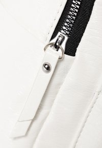 Witte gestructureerde faux leer met een zilveren rits en zwart stoffen detail, met een witte ritstrekker met een metalen accent.