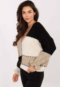Sweter rozpinany z dzianiny z poziomymi paskami w kolorach czarnym, beżowym i białym, głębokim dekoltem w serek oraz falbanianymi mankietami rękawów z małymi ozdobnymi guzikami.