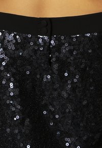 Svart paljettkjol med en slät midja som har två knappar. Tyget är tätt täckt av glänsande, runda paljetter som ger en texturerad effekt.