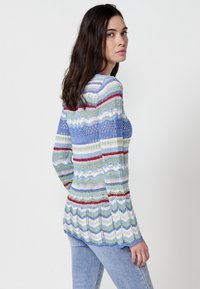 Strikket sweater med multicolor zigzag mønster i blå, grøn og rød. Har lange ærmer og en løs pasform, med ribbede detaljer.