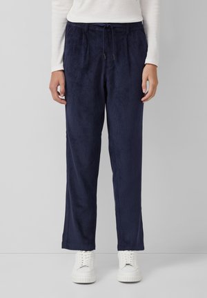 Marineblauwe corduroy broek met een elastische tailleband en trekkoorddetail, met wijde pijpen en een zachte textuur. Geselecteerd met witte sneakers.