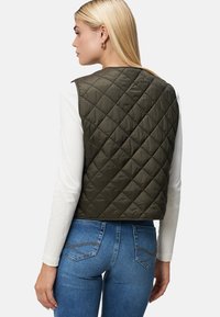 Gevoerde olijfgroene vest met een aansluitende pasvorm en een gladde textuur, gedragen over een wit langemouwen top. Heeft een ronde halslijn en geen sluiting aan de voorkant.