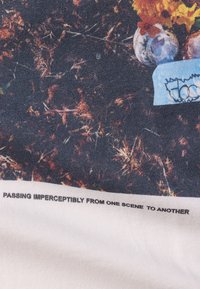 Tissu avec un fond sombre et texturé présentant des tons terreux et des motifs abstraits. Texte blanc indiquant : "PASSANT IMPERCEPTIBLE D'UNE SCÈNE À L'AUTRE."