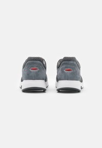 Graue Sneakers aus einer Kombination von strukturiertem Wildleder und Mesh, mit einer weißen Außensohle und einem roten Logodetail auf der Rückseite. Runde Form mit niedrigem Knöcheldesign.