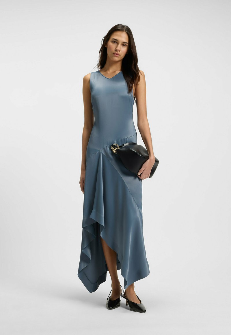 Blaues Satin-Kleid mit asymmetrischem Saum, das mit Drapierungen versehen ist. Kombiniert mit einer schwarzen Clutch und spitzen Absätzen.