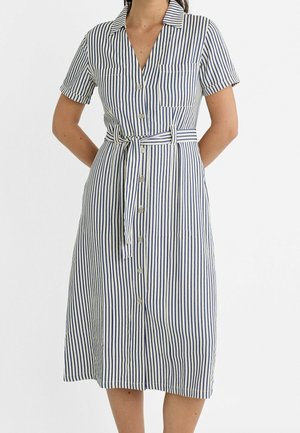 Woman wearing a short-sleeve, knee-length, blue and white vertical striped dress with buttons down the front and a tied waist belt.