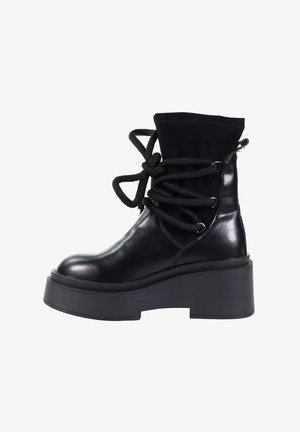 Czarne botki za kostkę z błyszczącą skórzaną powierzchnią, masywną czarną platformą oraz teksturowanymi czarnymi sznurowadłami owiniętymi wokół góry.