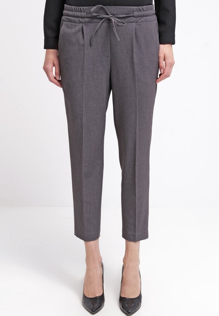 Pantalones grises a medida con cintura de cordón, pliegues frontales y pierna ajustada, combinados con zapatos de tacón negros. Tejido suave y texturizado.
