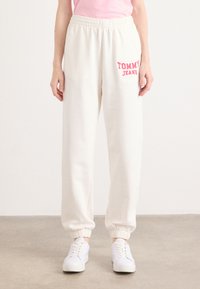 Crème sweatpants met elastische tailleband en boorden. Voorzien van een roze "TOMMY JEANS" logo aan de linkerkant. Gecombineerd met witte sneakers.