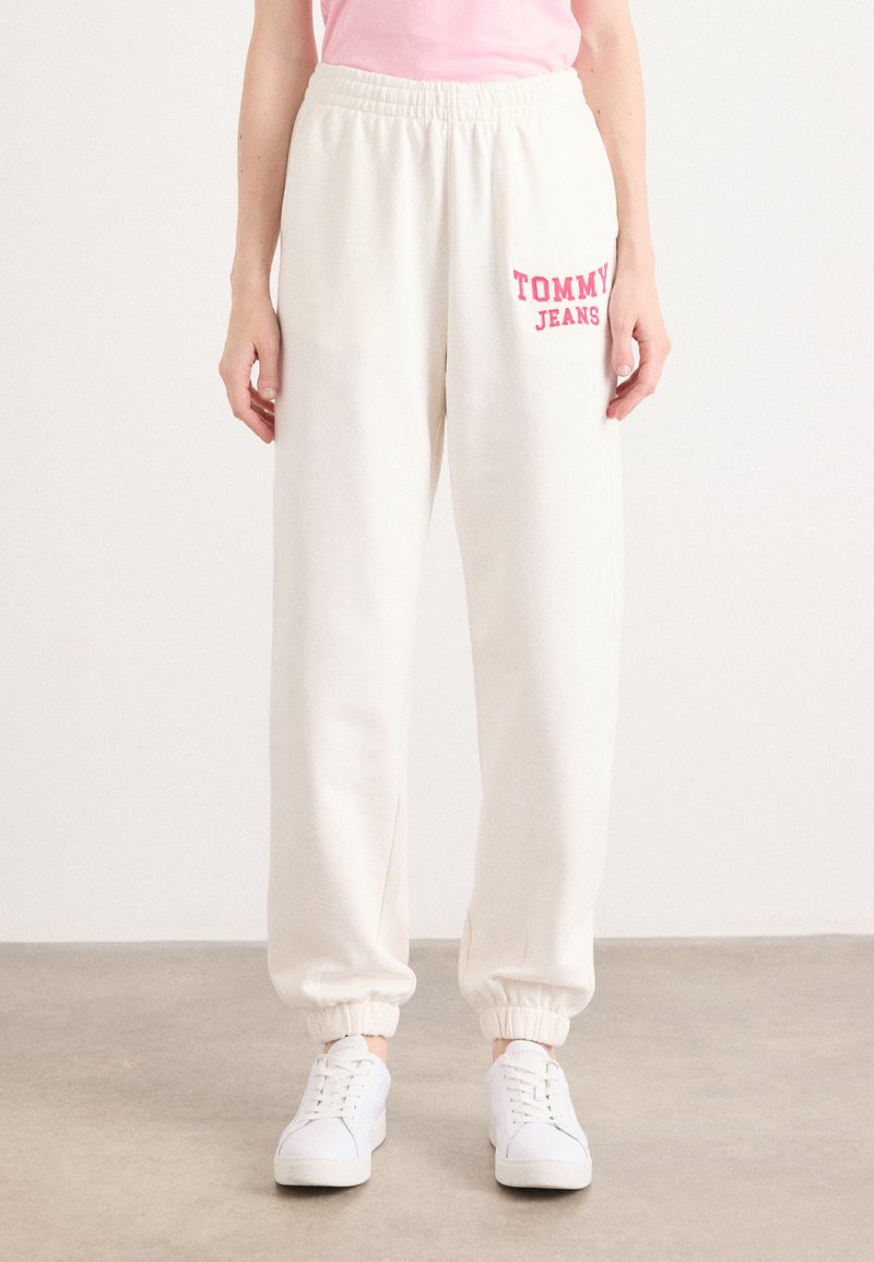 Crème sweatpants met elastische tailleband en boorden. Voorzien van een roze "TOMMY JEANS" logo aan de linkerkant. Gecombineerd met witte sneakers.