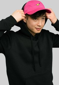 Czarna bluza z kapturem z kieszenią z przodu, w połączeniu z różową czapką z haftem małego ptaka. Bluza ma sznurki i miękką teksturę.