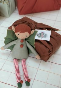 Stuffed doll with green dress, red buttons, and striped legs; next to a brown fabric-wrapped gift with a decorative tag.