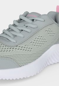 Chaussure de sport gris clair avec panneaux latéraux en mesh, lacets assortis, semelle blanche et une petite touche rose au talon.