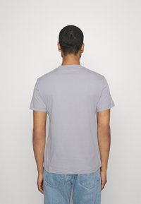 Camiseta de manga corta, de color gris claro, con cuello redondo, hecha de material de algodón suave. Presenta un corte relajado y un dobladillo limpio y recto.