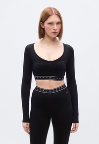 Μαύρο cropped τοπ με μακριά μανίκια και στρογγυλή λαιμόκοψη, με ρέλι κουμπιών και ελαστική ταινία με λογότυπο στο κάτω μέρος. Λείο υλικό.