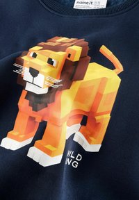 Granatowa bluza z grafiką pikselowego lwa w kolorach pomarańczowym, żółtym i brązowym. Z białymi akcentami oraz napisem "WILDING."