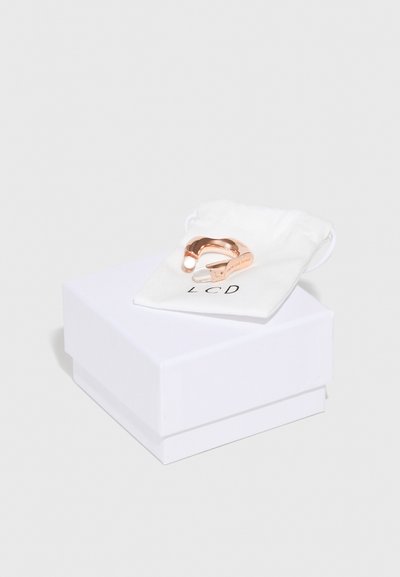 Et rose gullring vist på en hvit stoffpose, som hviler på en hvit gaveeske. Ringen har et jevnt, buet design.