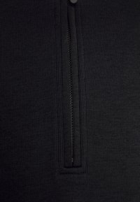 Černý zippered oděv s texturovanou pleteninou, který má vertikální zip na přední straně, jednotnou barvu a žádné další vzory.