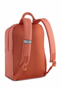 Sac à dos orange en tissu mesh, avec bretelles rembourrées et un logo en accent. Il présente une forme rectangulaire et une fermeture éclair pour le rangement.