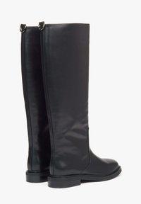 Vysoké černé kožené boty s plochou podrážkou a kovovým kroužkem na zadní části, stojící vedle sebe na bílém pozadí.