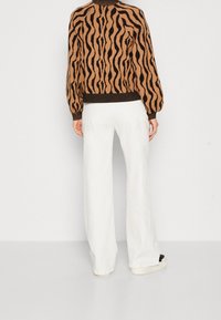 Stickad tröja i brunt och svart vågmönster, rundad halsringning, med åtsittande muddar. Matchad med vita vida byxor och casual sneakers.