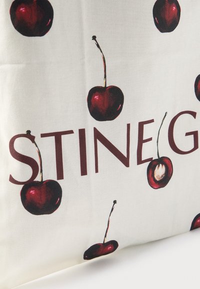 Cerises rouges avec tiges dispersées autour du texte partiel "STINE G" sur un tissu écru.