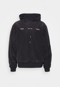 Sweat-shirt à capuche noir avec une texture légèrement froissée, présentant des détails en texte blanc et des poignets et un ourlet élastiques. Fermeture à glissière à l'avant.