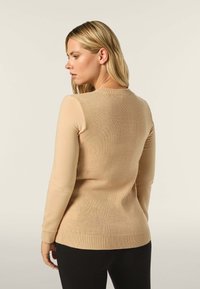 Beige Strickpullover mit Rundhalsausschnitt, langen Ärmeln und geripptem Saum, der eine glatte Textur und eine taillierte Silhouette aufweist.