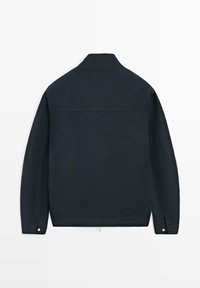 Veste noire à manches longues vue de dos avec un col montant et des poignets boutonnés sur fond blanc.