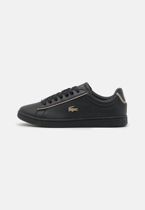 Baskets basses noires avec lacets noirs, logo crocodile doré sur le côté et détails dorés au talon et le long des lacets.