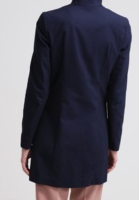 Abrigo largo azul marino con un cuello alto y mangas largas, hecho de una tela suave. Corte entallado sin adornos visibles.