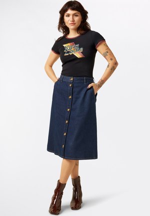 La gonna midi in denim presenta una chiusura con bottoni frontali, tasche laterali e un colore blu scuro. Abbinata a una maglietta grafica nera e stivaletti alla caviglia marroni.