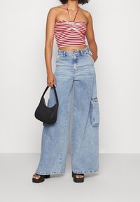 Top corto a righe rosse e bianche con collo all'americana, abbinato a jeans in denim azzurro chiaro a gamba larga con tasche laterali. Borsa nera con texture e scarpe con plateau.